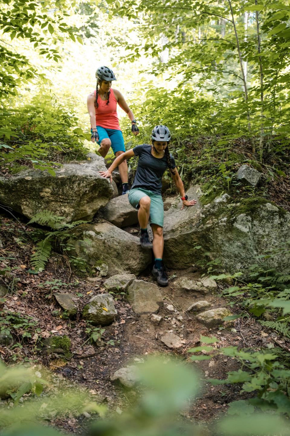Two women in mountain bike gear clamber down a rocky trail.