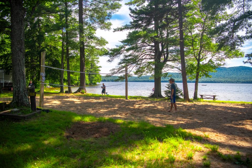 Young people playing beach volleyball at a campground with a lake and mountains in the background.
