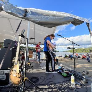 A band playing under a pop-up tent to a crowd at the Long Lake public beach