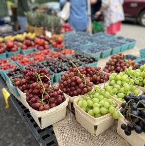 a table with a variety of fruit- grapes, berries, cherries, in pint size containers