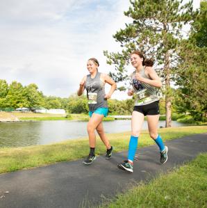 Two girls running in a race, on a path with a creek beside the path on a nice day in the summer