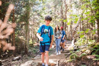 a family hiking on a trail in the forest&#44; a young boy leads the way with his mom and dad following behind him