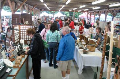 Many tables and booths set up for a craft fair with people walking around and looking at the items for sale on the tables