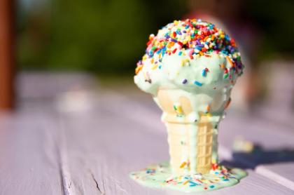 An ice cream cone on a table with the ice cream melting down the side