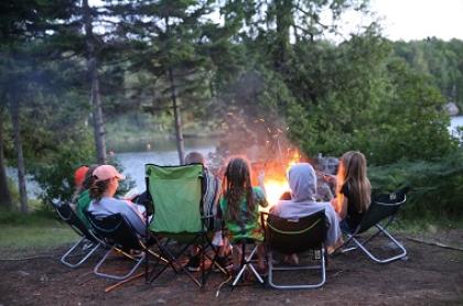 A family sits in camp chairs around a campfire at Forked Lake Campground