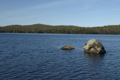 A couple large rocks sticking out of a pond.