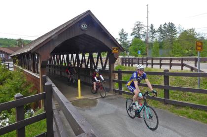 People bike over a small covered bridge