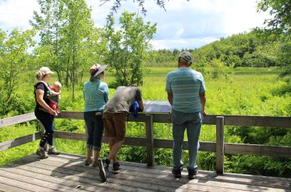 A group of people at a deck with interpretive signage on a trail