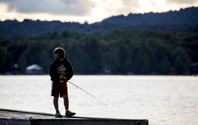 A boy in a hoodie and shorts fishes off of a dock in the early morning.