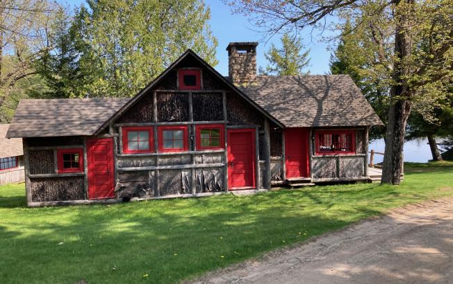 A wood cabin with rustic red trim on the sides with a green yard surrounding it.