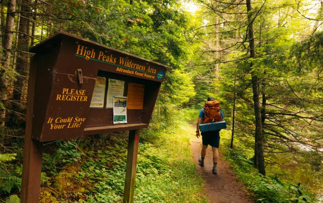A man walks past a High Peaks Wilderness sign on green trail