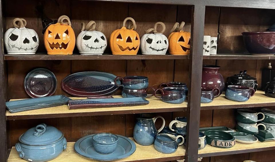 Wooden shelves hold handcrafted pottery mugs, bowls, and jack-o-lanterns.