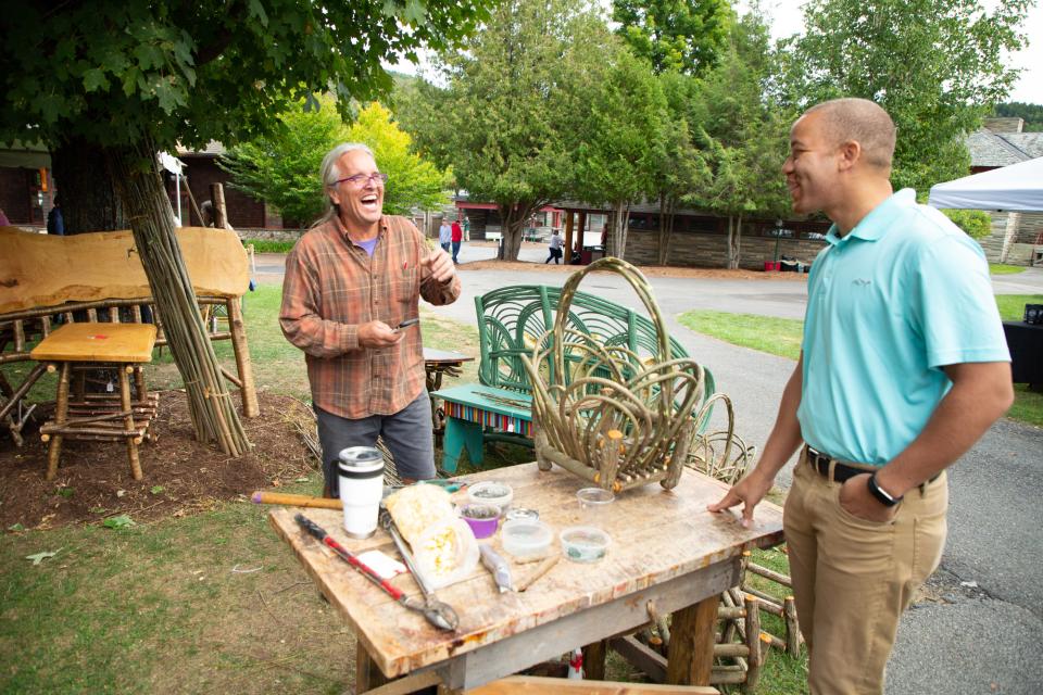 Two men laugh over an outdoor table where Adirondack rustic furniture is being built.