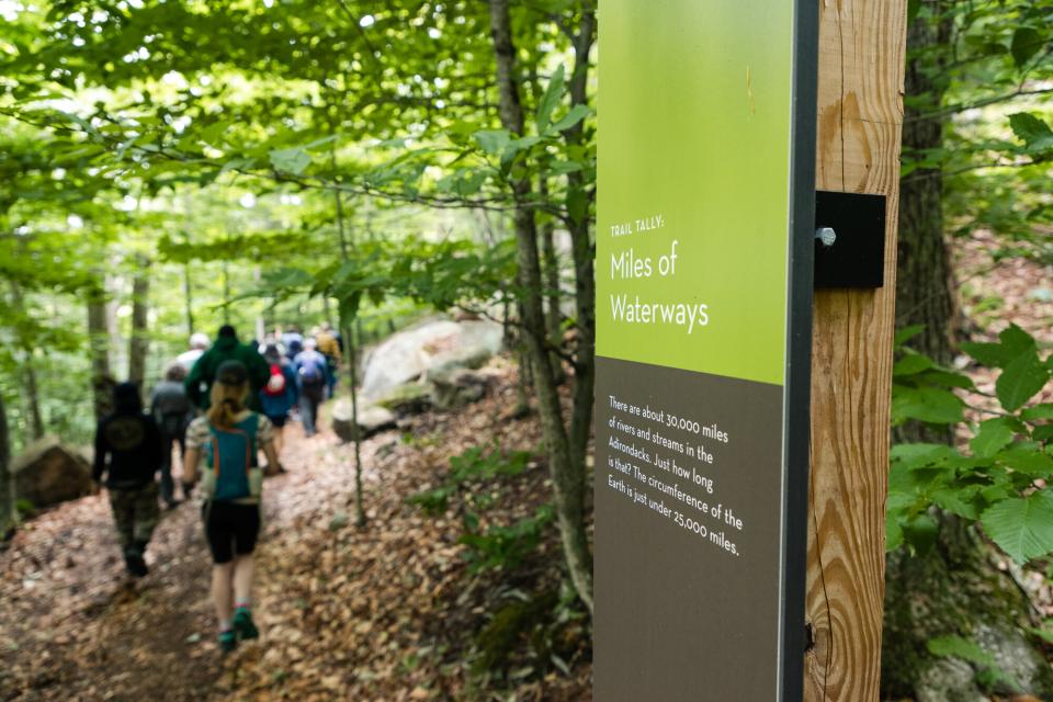 people walk past a sign on a hiking trail.