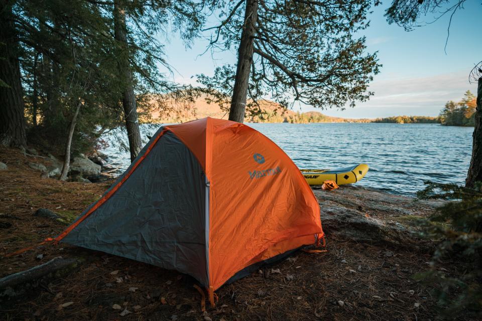 an orange tent sits on the shoreline of a lake.