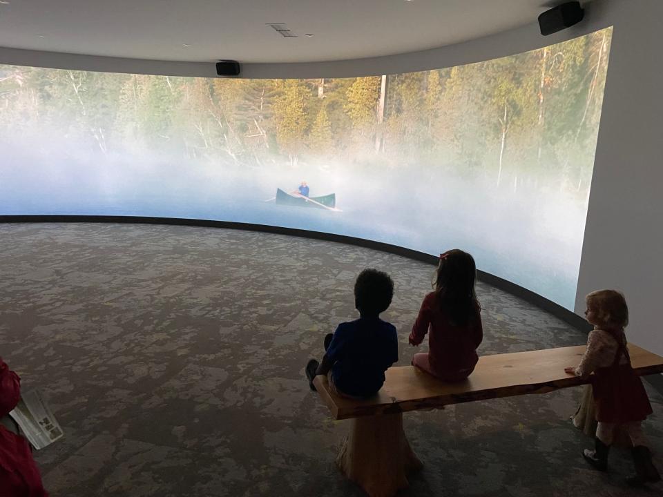 Three children sitting on a bench watching one of the exhibits screen presentations