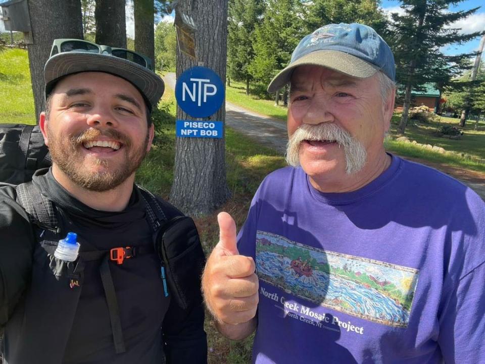 Two men smile in front of a "Piseco NPT Bob" sign