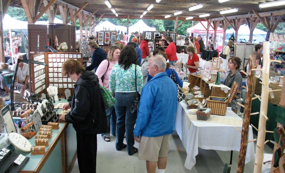 Many tables and booths set up for a craft fair with people walking around and looking at the items for sale on the tables
