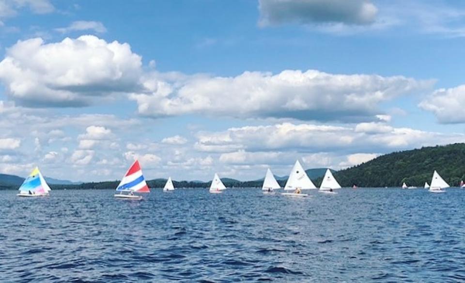 piseco lake with several sailboats on the water with a blue sky above with big puffy white clouds