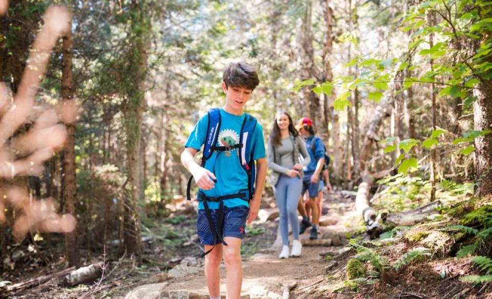 a family hiking on a trail in the forest, a young boy leads the way with his mom and dad following behind him