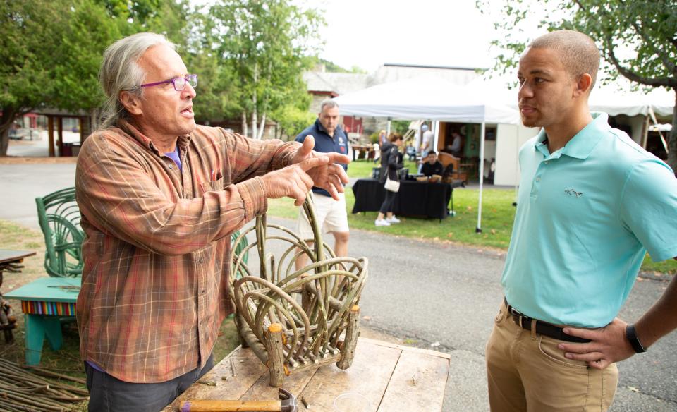 Two men talking, one man is an artisan making furniture from twigs and thin branches and the other man visiting the vender and listening