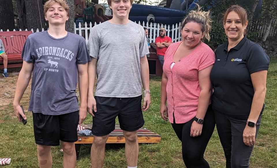 Four people pose in front of a cornhole board