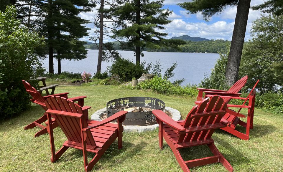 Adirondack Chairs circling a fire pit overlooking the lake through the trees