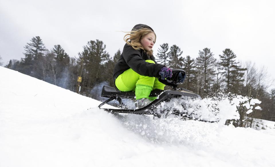 A young kind heading down a hill on a snow sled